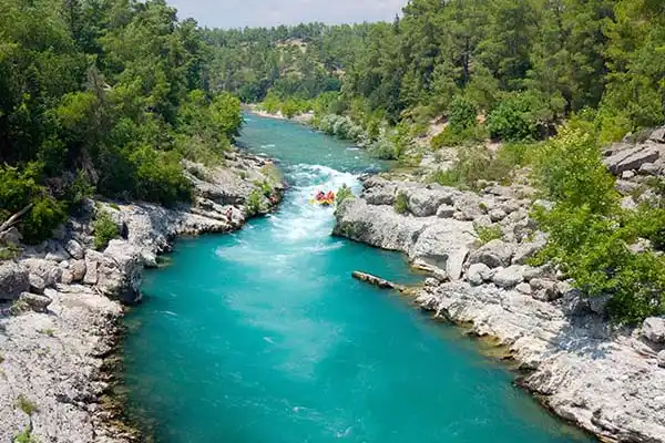 High-angle view of a yellow raft navigating a turquoise river winding through a narrow rocky canyon with lush green trees