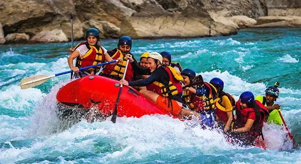 A blue raft with six paddlers hitting a large white-water wave head-on