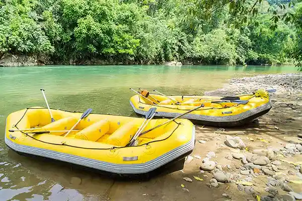 Two yellow inflatable rafts with oars resting on a rocky riverbank next to calm clear water